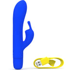 Vibromasseur rabbit bleu roi dressé à gauche, câble de charge jaune enroulé à droite. Tige courbée et oreilles externes en silicone satiné, double moteur, coloris électrique.