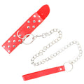Sangle de collier rouge à rivets et anneau, reliée à une laisse à chaîne argentée et poignée rouge, présentée en diagonale, élément du collier de soumission BDSM.