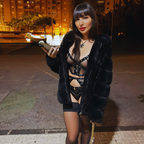 Aya Benetti debout de nuit en rue eclairee, manteau ouvert sur de la lingerie noire lacee, pose audacieuse et regard direct dans une ambiance urbaine nocturne