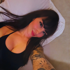 Aya Benetti en portrait rapproche allongee, longue chevelure brune et regard doux face camera, tatouage sur l'avant-bras, lumiere naturelle et atmosphere intime