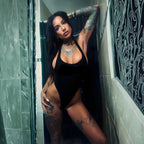 InkNikky debout en body noir echancre dans une salle de bain carrelee, tatouages apparents et pose sensuelle, regard direct camera dans une lumiere froide