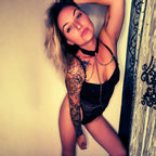 Liv_8457 posant bras leve en body noir avec collier ras-de-cou, bras tatoue, regard intense et pose sensuelle dans une lumiere doree chaude exterieure