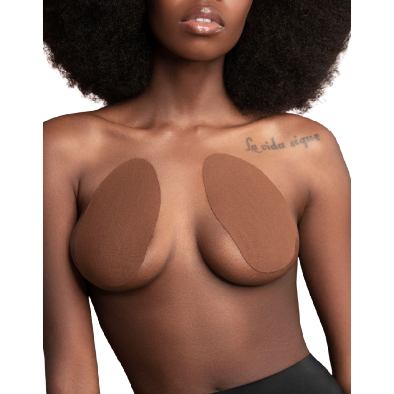 Coussinets de lifting des seins Bye Bra coloris marron portes de face, patchs adhesifs ovales en coton remontant la poitrine, demonstration sur modele a la peau foncee, jupe noire