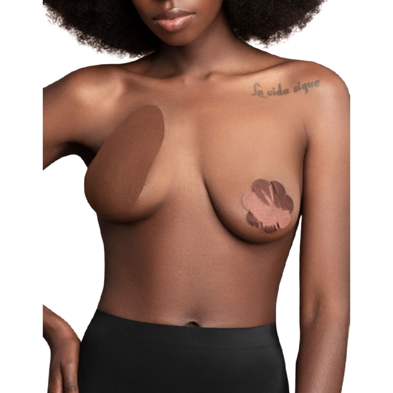 Couvre-mamelon petale satine Bye Bra coloris marron pose sur le sein, pastille fleur adhesive protegeant le teton, demonstration de pose sur modele a la peau foncee buste, jupe noire taille basse