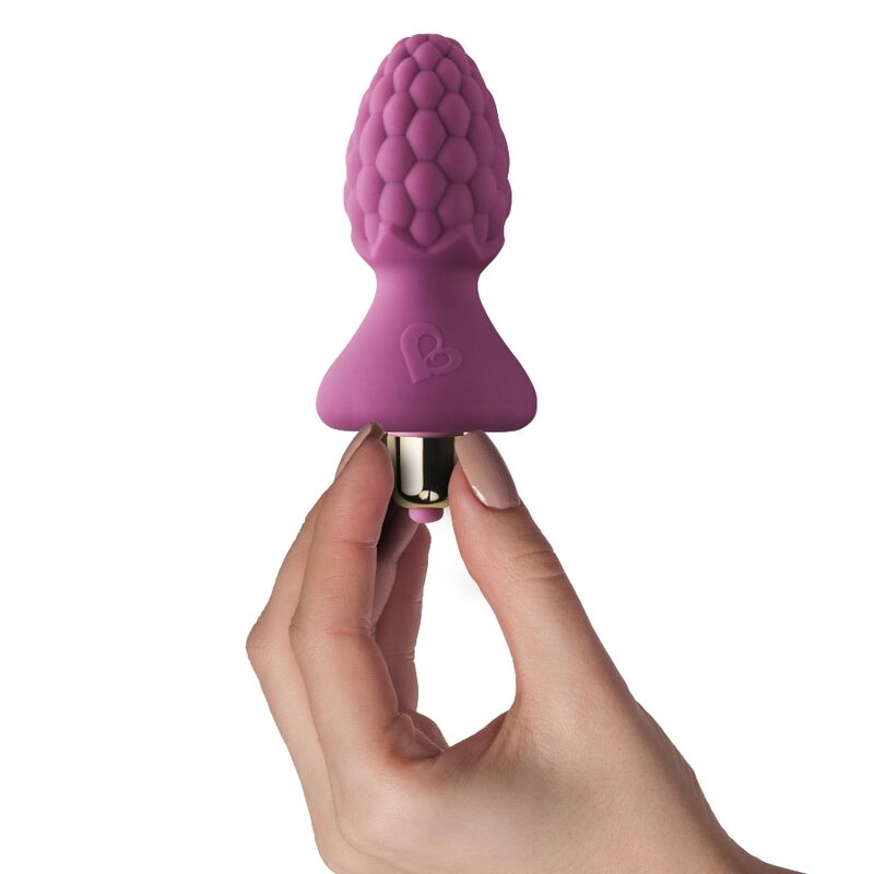 Main féminine tenant le plug anal framboise rose par sa base en T, tête granuleuse visible, illustrant le petit gabarit du jouet anal en silicone texturé rose vif.