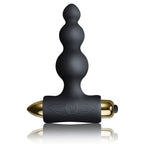 Plug anal noir à tige perlée de billes étagées sur base en T, capsule vibrante dorée logée dans le socle, silicone mat lisse, format du pack Silhouette.