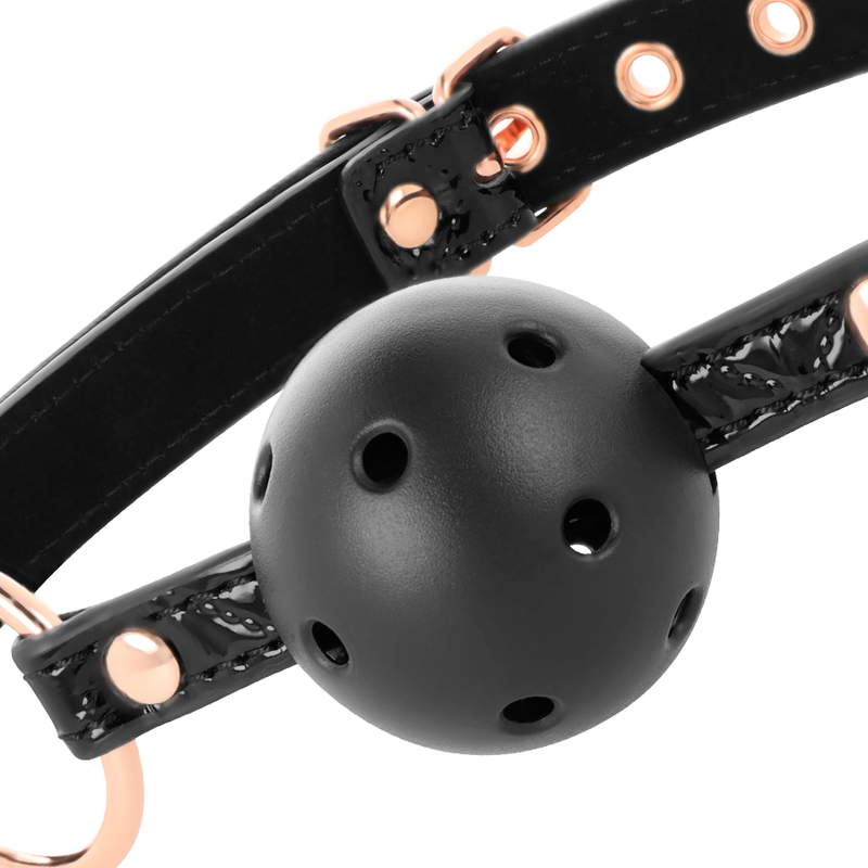 Gros plan sur la boule perforée noire et le serre-tête à oeillets or rose du bâillon Begme, accessoire BDSM réglable bouton-pression.