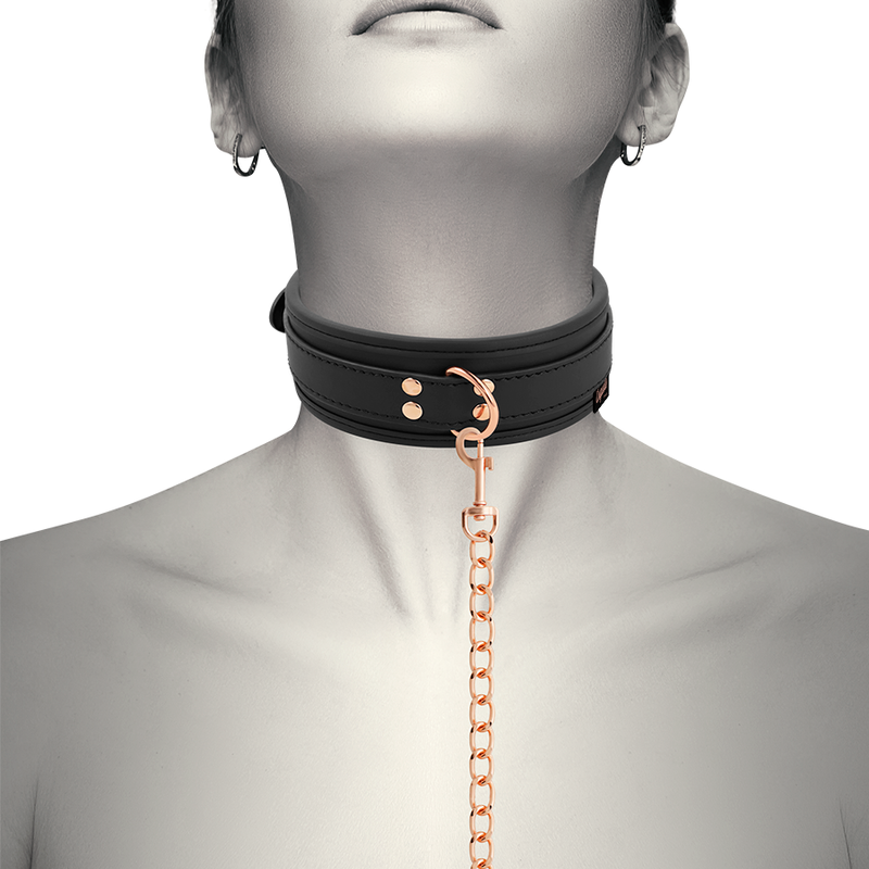 Collier cuir vegan noir Coquette avec laisse a chaine or rose porte au cou d'un modele, accessoire de soumission BDSM relie a une laisse pour jeux de domination.