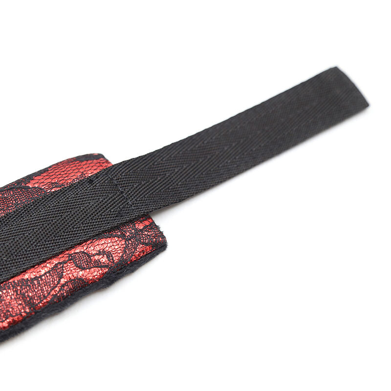 Detail rapproche d'une manchette velours a dentelle rouge a sangle velcro repliee, montrant la fermeture reglable confortable d'une attache de poignet pour le bondage soft.