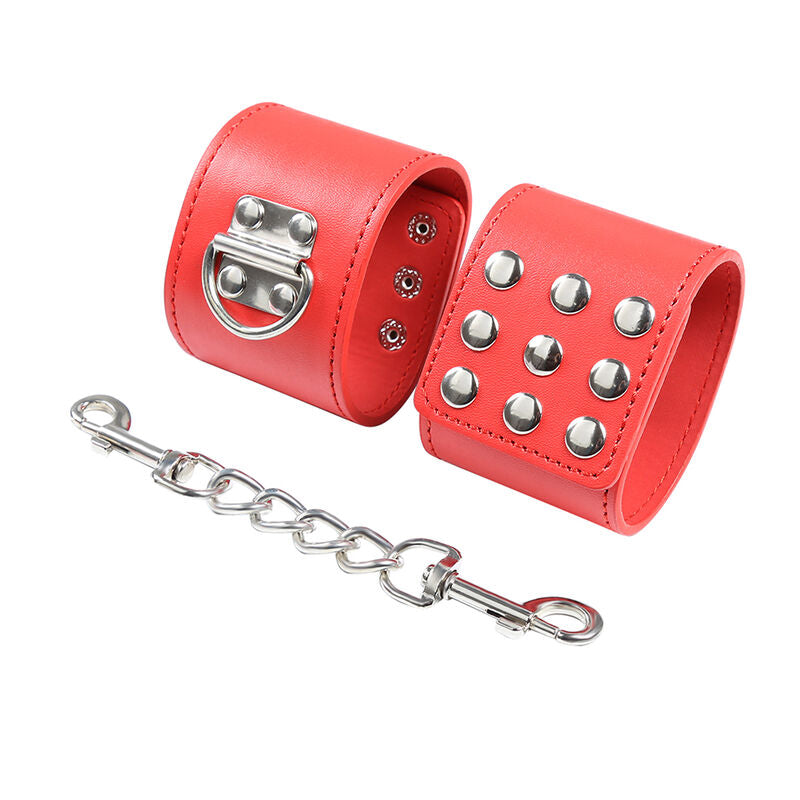 Menottes de poignets en cuir rouge cloute reliees par une chaine metallique a mousqueton, fermeture D-ring vue rapprochee, accessoire de contention au look affirme.