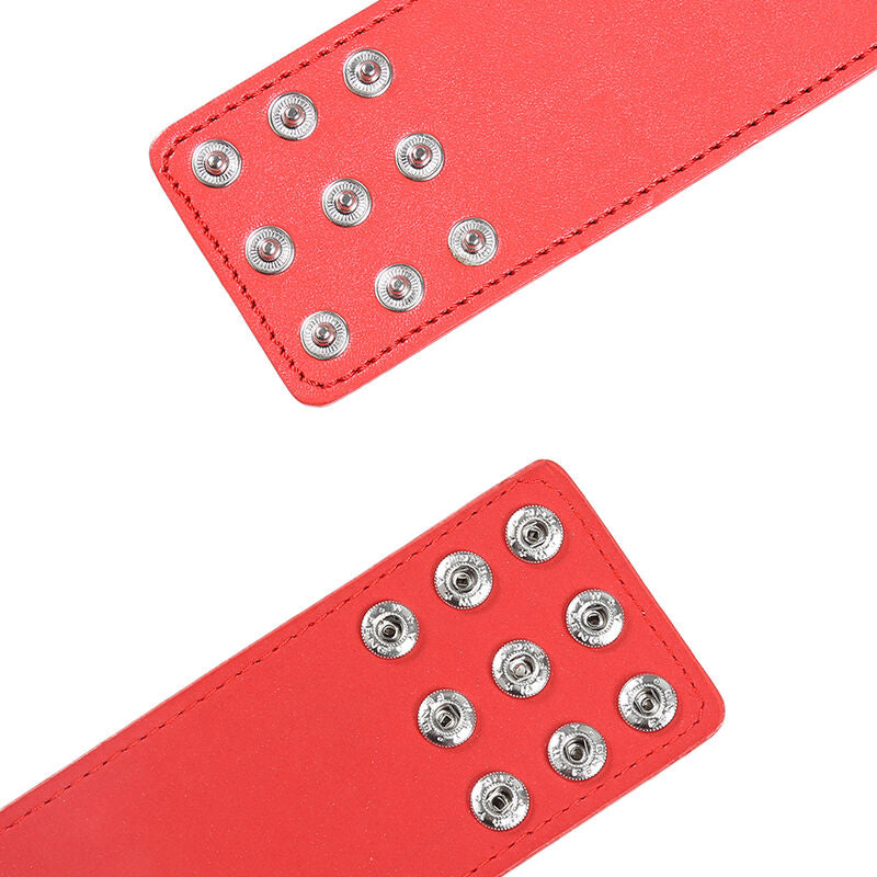 Detail de manchettes en simili cuir rouge ornees de clous metalliques, montrant la finition cloutee et les coutures soignees d'une attache de poignet BDSM resistante.