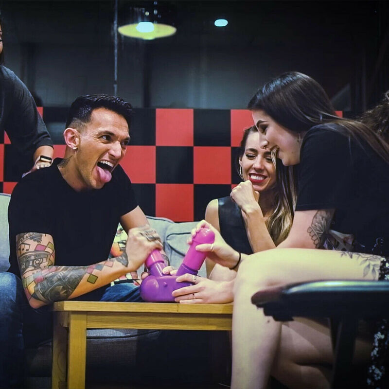 Scene de soiree EVJF avec invites riant autour d une table, manipulation du jeu Cum Face violet et rose, ambiance jeu humoristique en duel pour enterrement de vie
