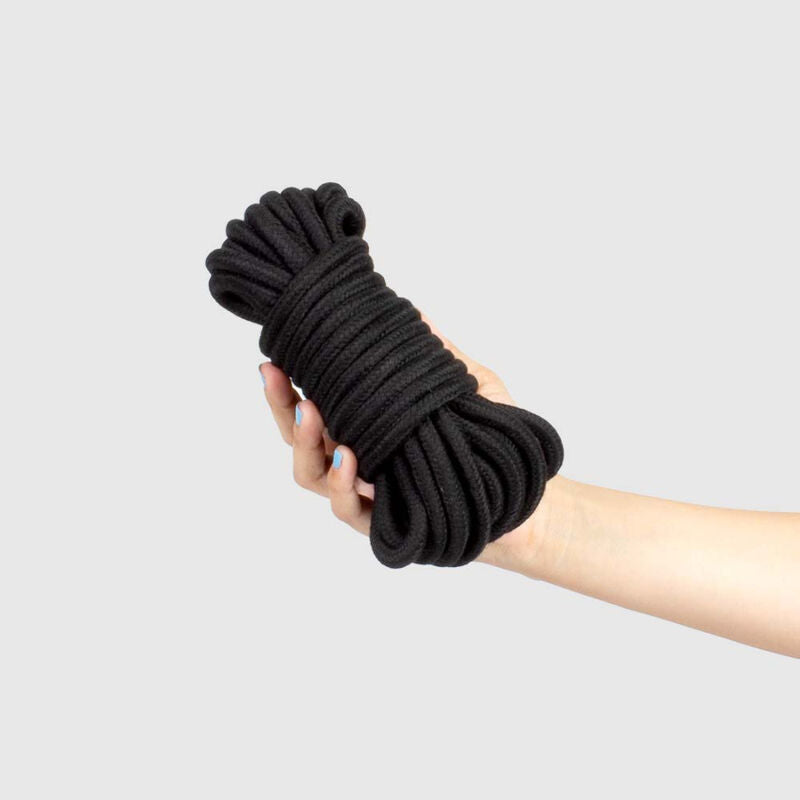 Corde de bondage shibari Secretplay noire pelotonnee tenue dans une main, 10 metres de coton et polyester soyeux pour varier les nouds de bondage.