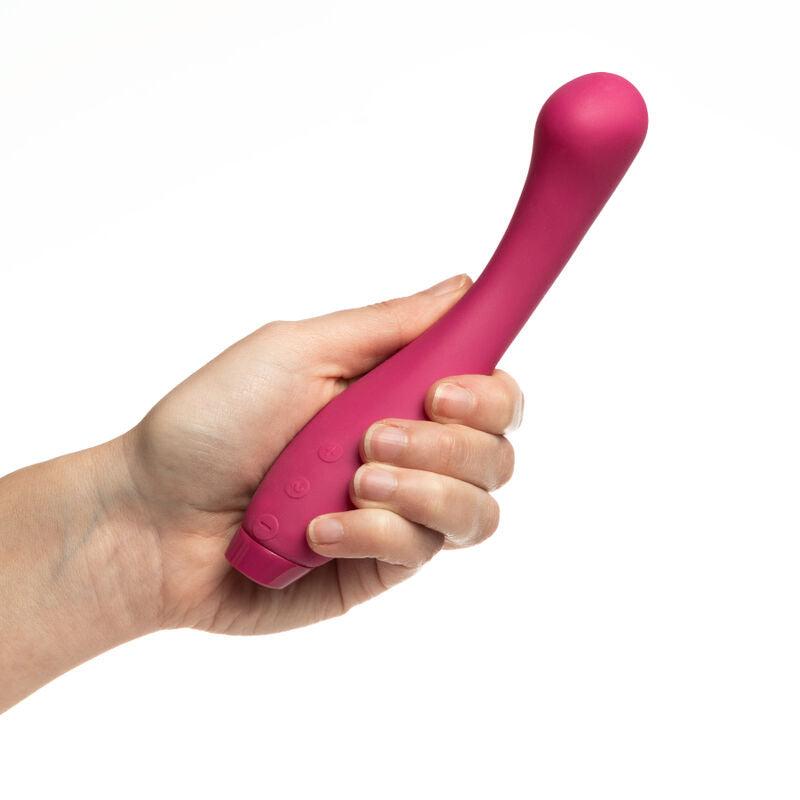 Vibromasseur point G Juno rose saisi à pleine main, tige incurvée à embout incliné dépassant des doigts repliés, plan de prise rapproché du produit sur fond blanc parfaitement épuré.