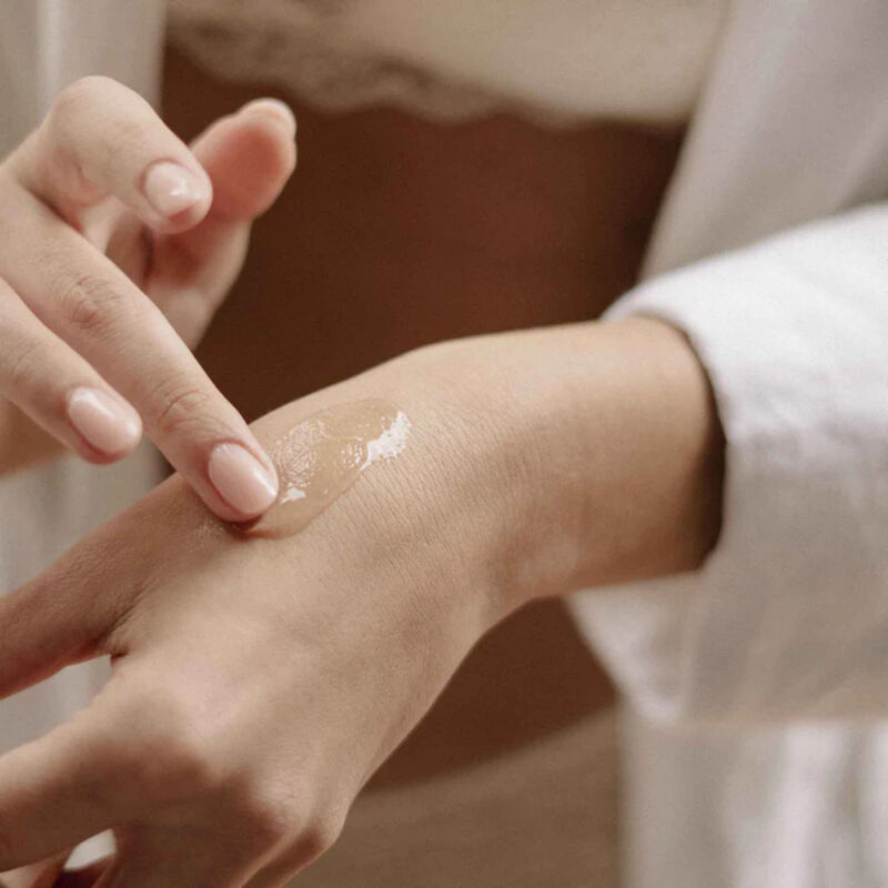 Application du serum Sex au Naturel Bijoux Indiscrets sur le dos de la main, gros plan sur les doigts etalant le soin, demonstration de la texture du serum clitoridien