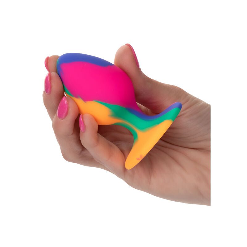 Plug anal Cheeky en silicone tie-dye multicolore tenu en main, mise à l'échelle du corps souple et de la base ventouse de ce plug moyen pour débutant·e·s.