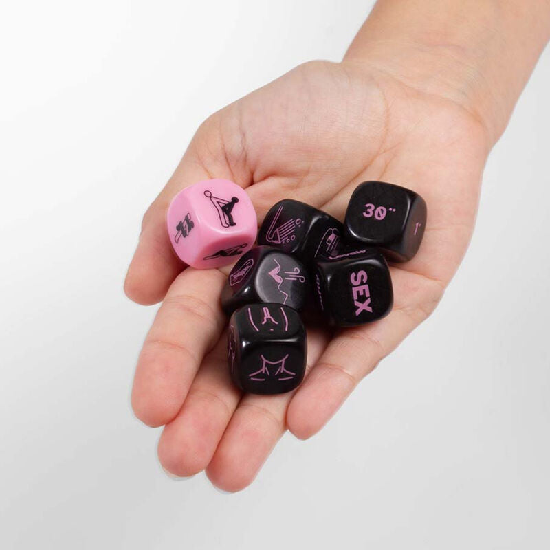 Des coquins Dice Play Sex Secretplay roses et noirs graves tenus dans une paume, jeu de des positions et actions pour relancer la complicite a deux.