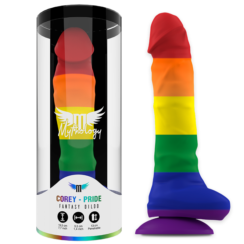 Gode Corey Pride Mythology arc-en-ciel a la forme penienne avec testicules moules, presente dans son tube cylindrique et pose a cote, base ventouse violette