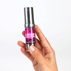 Flacon airless rose Liquid Vibrator Hot tenu dans une main, gel stimulant Secret Play effet chaud fraise creme, gros plan presentant le format compact du produit.