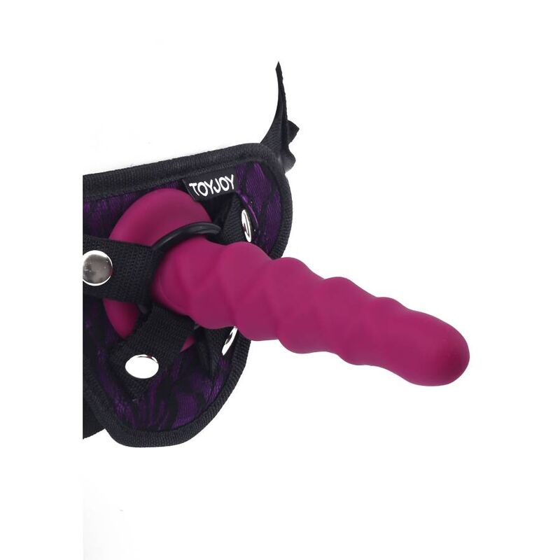 Gode cotele fuchsia en silicone monte sur un harnais Toy Joy violet, vue de trois quarts. Relief nervure non realiste fixe a la sangle reglable pour strap-on.