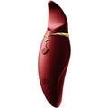 Vibromasseur clitoridien Hero rouge bordeaux de trois quarts, liseré doré et pampille en éventail, corps galbé lisse en silicone, finition satinée élégante.