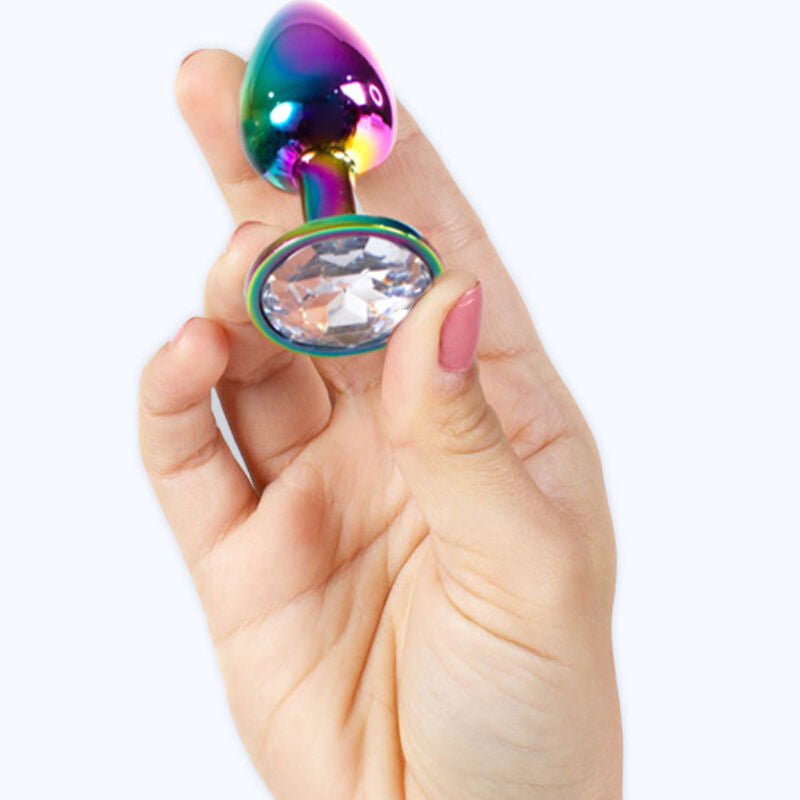 Plug anal bijou metal irise arc-en-ciel a base strass tenu entre les doigts, demonstration de la taille compacte de l accessoire lisse Plug and Play.