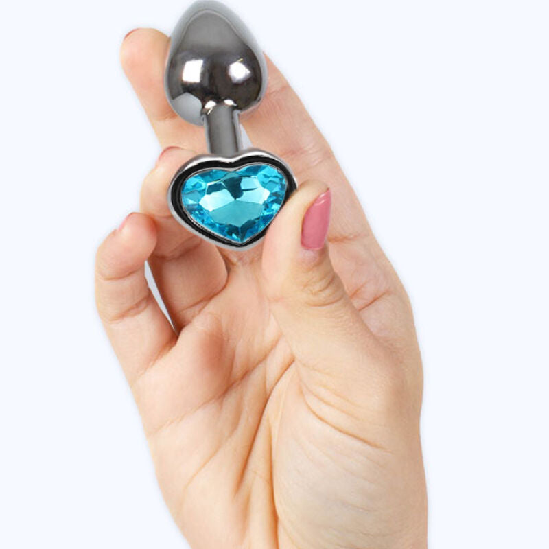Plug anal bijou metal a base coeur strass bleu tenu entre les doigts, demonstration de la petite taille de l accessoire lisse Plug and Play Secret Play.