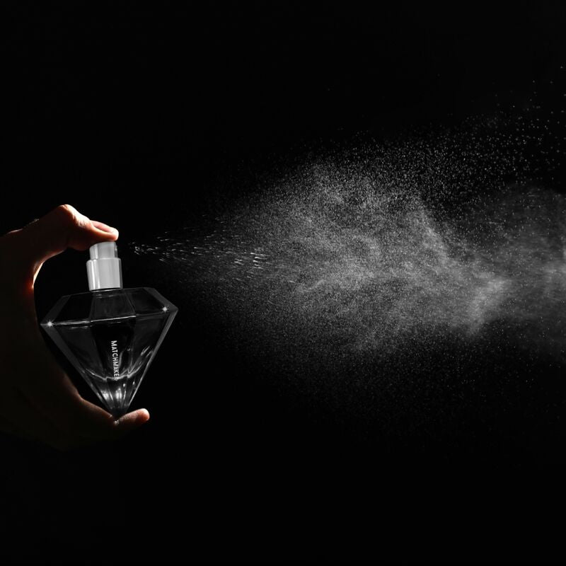 Flacon diamant noir du parfum aux phéromones Matchmaker Black Diamond vaporise sur fond noir, nuage de brume visible, eau de parfum facette a bouchon cristal Eye Of Love.
