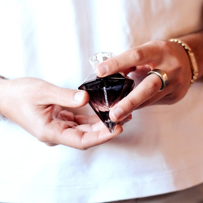 Flacon diamant noir du parfum phéromones Matchmaker Black Diamond tenu dans deux mains, bouchon cristal pres du flacon facette, eau de parfum boisee pour lui Eye Of Love.