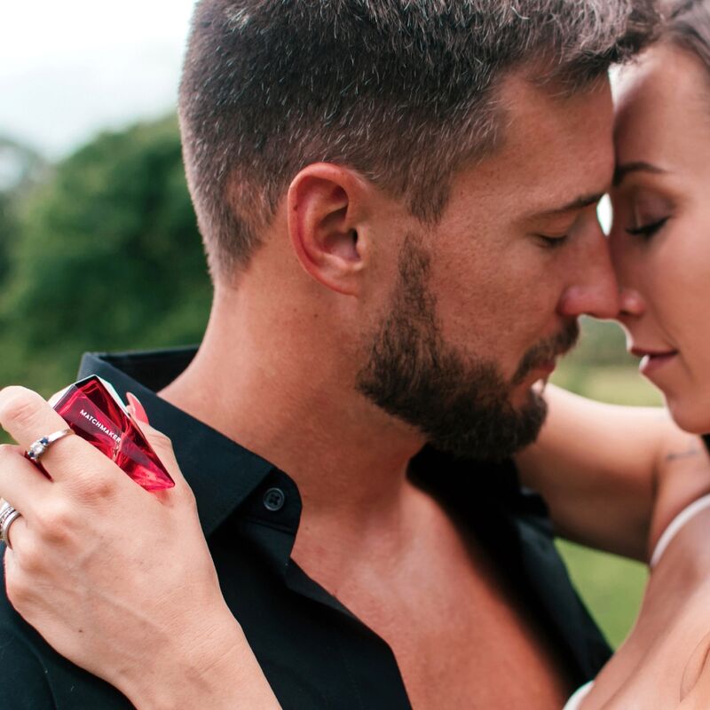 Couple habille enlace en exterieur, la femme vaporise le parfum aux phéromones Matchmaker Red Diamond, flacon diamant rouge en main, scene romantique Eye Of Love.
