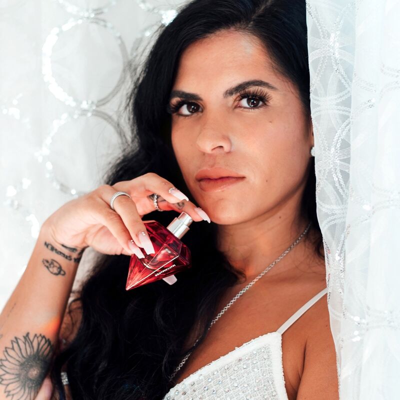 Femme brune en haut blanc tenant le flacon diamant rouge du parfum aux phéromones Matchmaker Red Diamond, eau de parfum a bouchon cristal, portrait glamour Eye Of Love.