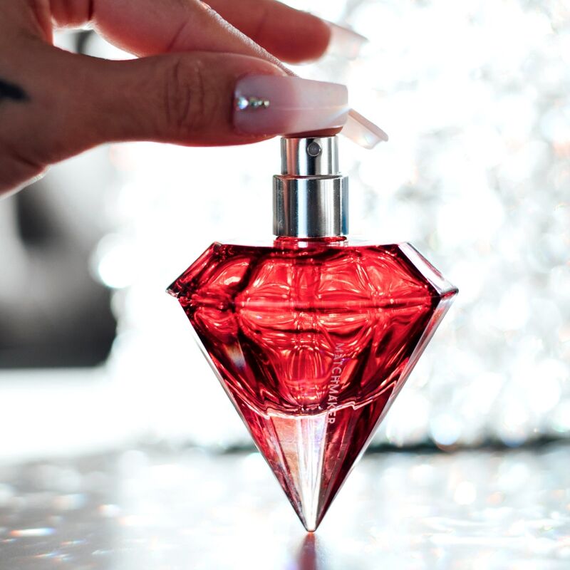 Flacon diamant rouge du parfum aux phéromones Matchmaker Red Diamond tenu entre les doigts, eau de parfum facette a bouchon cristal vaporisee, fond scintillant Eye Of Love.