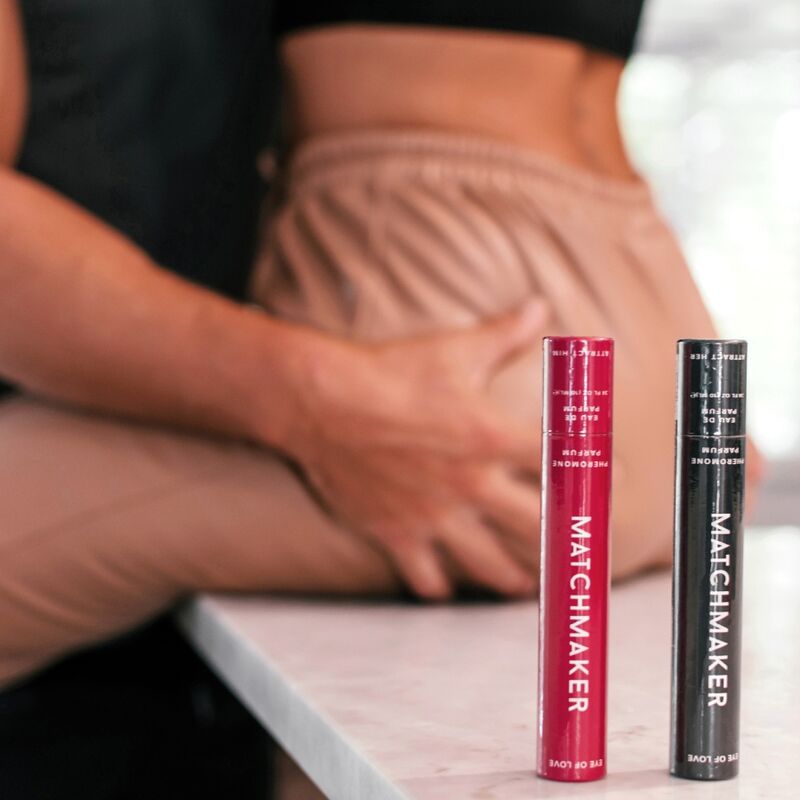 Deux sticks roll-on Matchmaker rouge et noir aux phéromones poses pres d'une personne habillee, eau de parfum nomade Black Diamond et Red Diamond Eye Of Love.