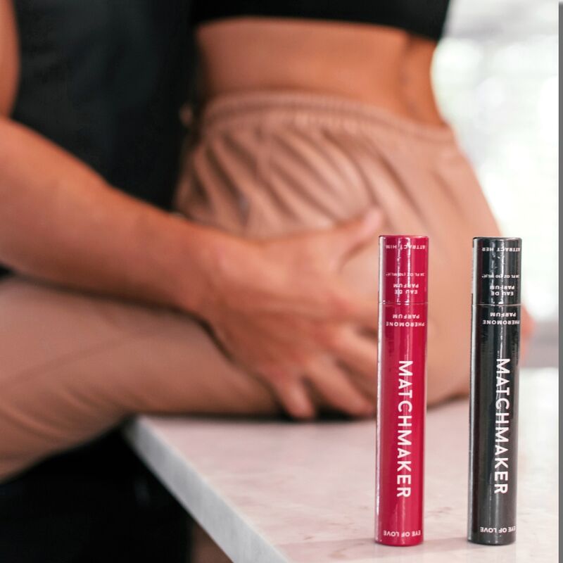 Deux roll-on Matchmaker Red Diamond aux phéromones poses sur un plan, mains d'un couple habille en arriere-plan, eau de parfum jasmin pamplemousse ambre Eye Of Love.