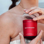 Personne aux epaules denudees tenant la bougie de massage rouge Matchmaker, mise en situation intime du soin aux pheromones 150 ml Eye Of Love.