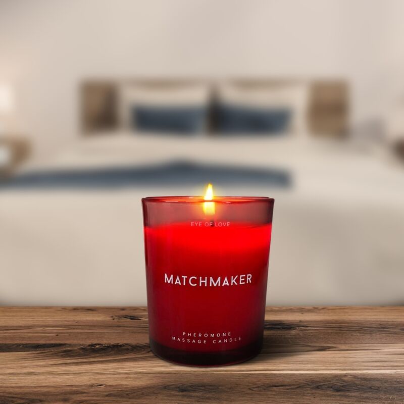 Bougie de massage rouge Matchmaker allumee posee sur une table en bois, ambiance chambre tamisee, soin aux pheromones 150 ml beurre de karite Eye Of Love.
