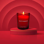 Bougie de massage rouge Matchmaker allumee sur socle dans un decor concentrique rouge, ambiance chaleureuse du soin aux pheromones 150 ml Eye Of Love.