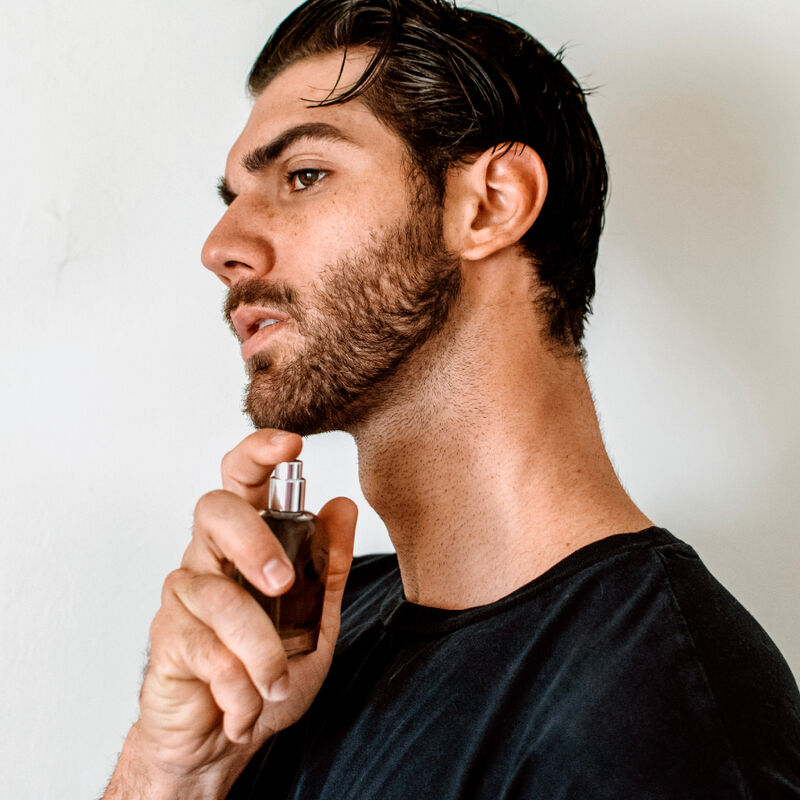Homme barbu en haut noir vaporisant le parfum Romantic sur son cou, mise en situation du parfum aux pheromones pour homme 50 ml Eye Of Love.