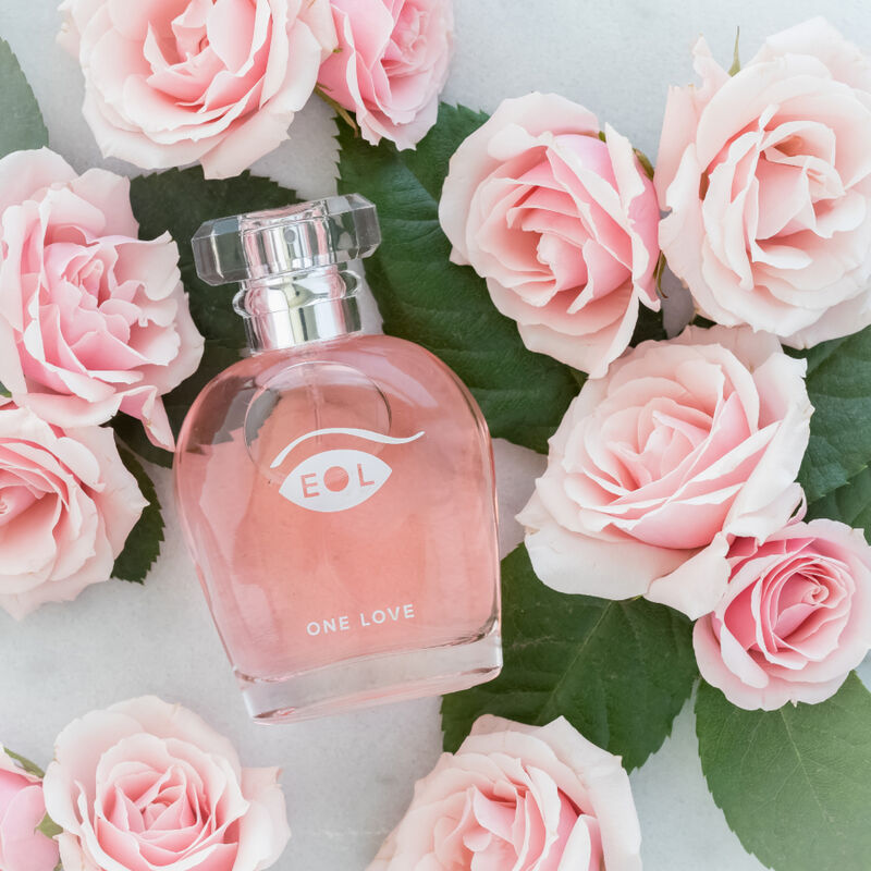 Flacon rose One Love mis en scene parmi des roses pales, parfum aux pheromones pour femme 50 ml composition florale jasmin rose lys Eye Of Love.
