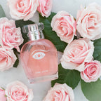 Flacon rose One Love mis en scene parmi des roses pales, parfum aux pheromones pour femme 50 ml composition florale jasmin rose lys Eye Of Love.