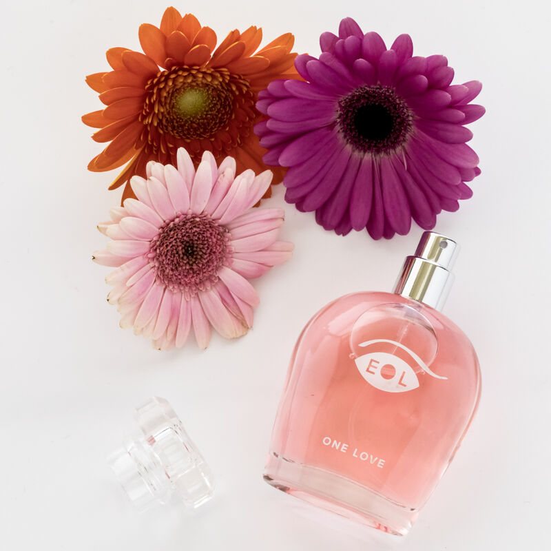 Flacon rose One Love pose pres de fleurs colorees, mise en scene fraiche du parfum aux pheromones pour femme 50 ml floral et sensuel Eye Of Love.