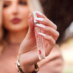 Femme aux ongles clairs tenant le roll-on One Love rose pres du visage, gros plan sur le parfum aux pheromones pour femme 10 ml Eye Of Love.