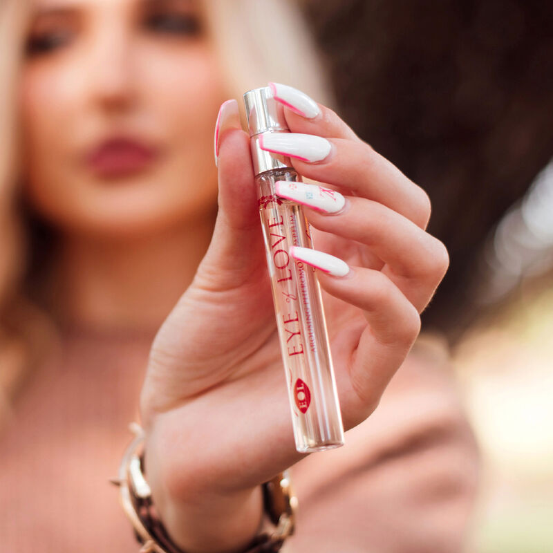 Femme aux ongles clairs tenant le roll-on One Love rose pres du visage, gros plan sur le parfum aux pheromones pour femme 10 ml Eye Of Love.