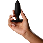 Plug Onyx noir facetté tenu dans une main aux ongles clairs, base recourbée bien visible, plan de prise illustrant la taille et le confort du plug en silicone sur fond blanc épuré.