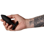 Plug anal Onyx noir tenu entre les doigts d'une main tatouée, pointe facettée dirigée vers la gauche, échelle de taille mise en avant sur fond blanc épuré, plan de prise rapproché.