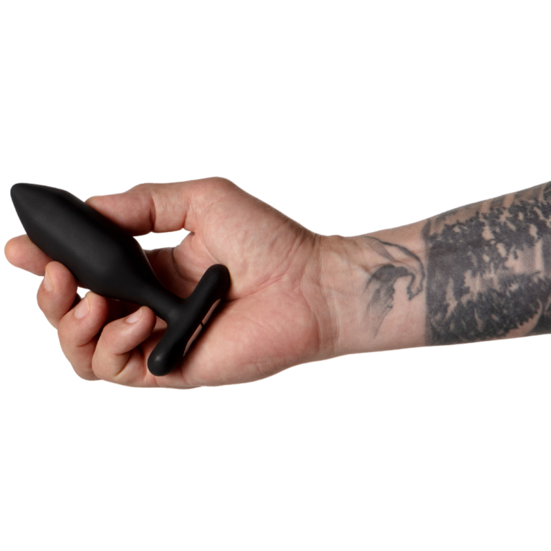 Plug anal Onyx noir tenu entre les doigts d'une main tatouée, pointe facettée dirigée vers la gauche, échelle de taille mise en avant sur fond blanc épuré, plan de prise rapproché.