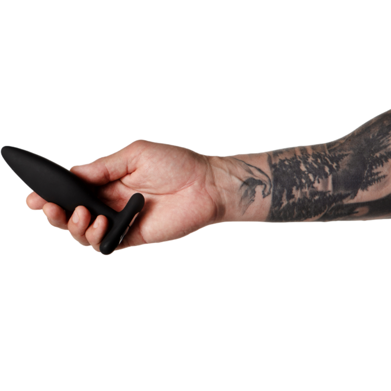 Vibrateur anal Egon noir tenu entre les doigts d'une main tatouée, pointe effilée dirigée vers la gauche, échelle de taille mise en évidence sur fond blanc épuré, plan rapproché.