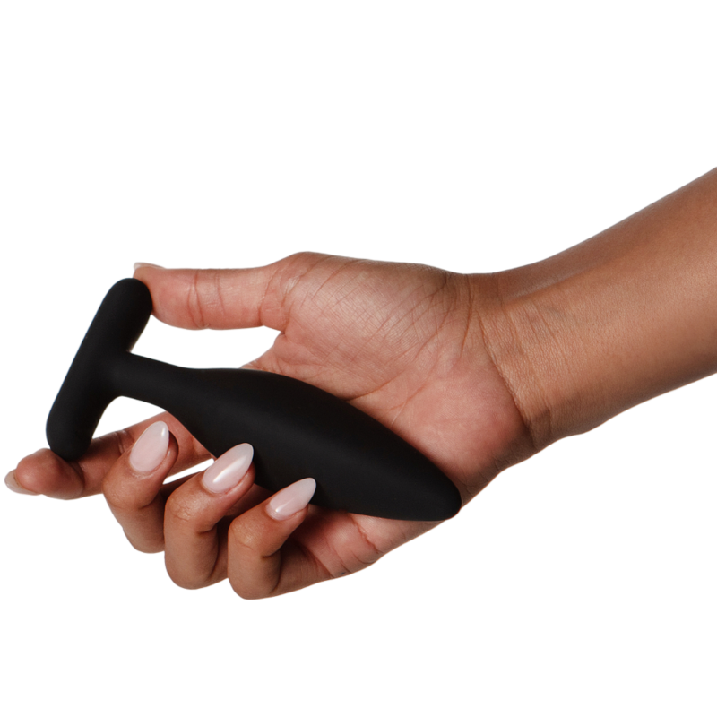 Plug Egon noir tenu dans une main aux ongles manucurés, base recourbée bien visible entre les doigts, plan montrant la prise et la taille de l'objet lisse en silicone sur fond blanc.