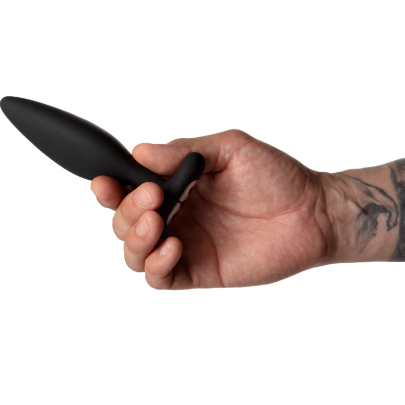 Plug anal Vesta noir tenu entre les doigts d'une main tatouée, l'objet lisse en forme de goutte met en évidence sa petite taille, plan de prise rapproché sur fond blanc épuré.
