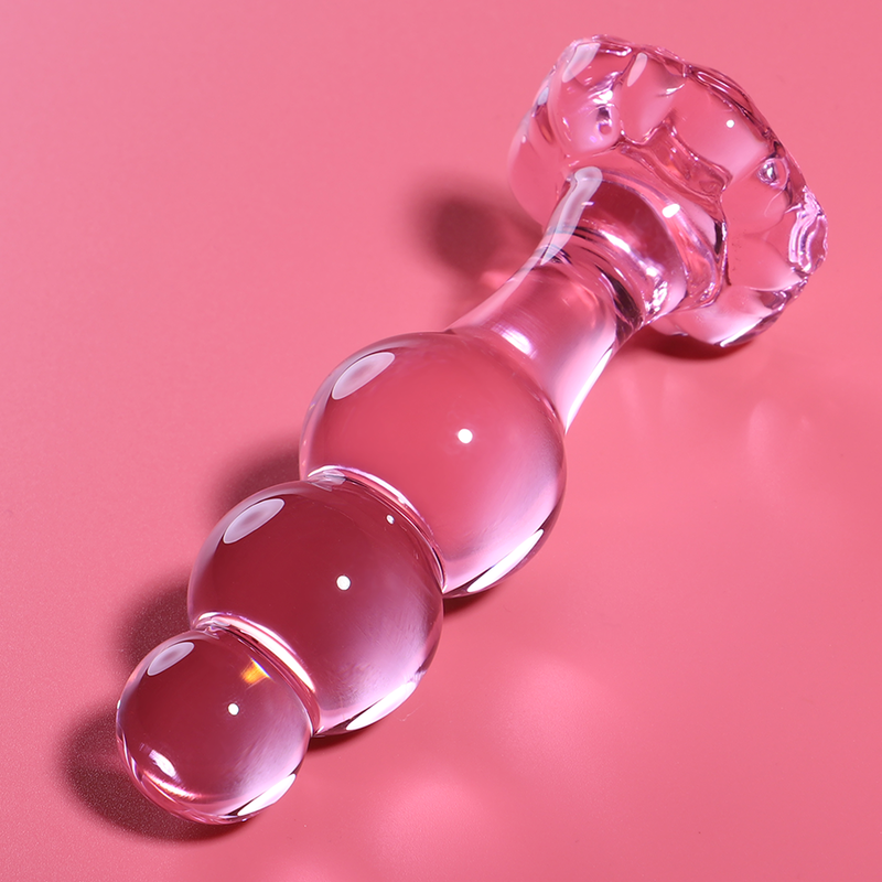 Plug anal en verre borosilicate rose pose en diagonale sur fond rose, perles brillantes et base fleur evasee, surface lisse pour un jeu de temperature doux.
